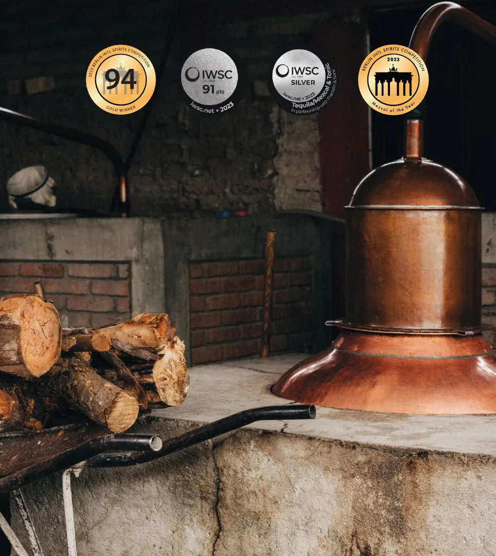 Zwei Kupferdistillen. Davor eine Schubkarre mit Holz. Dazu vier Awards, die der Mezcal Laepoca gewonnen hat.
